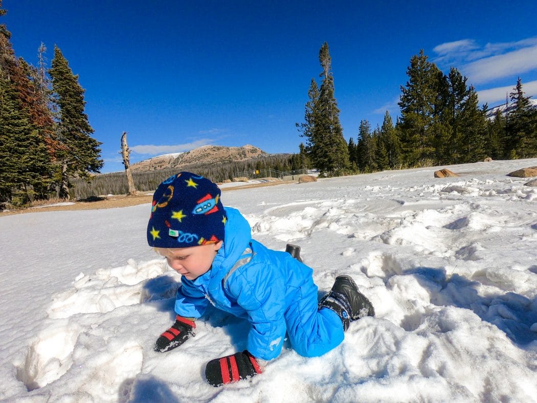 baby crawling in snow wearing mittens and snow boots