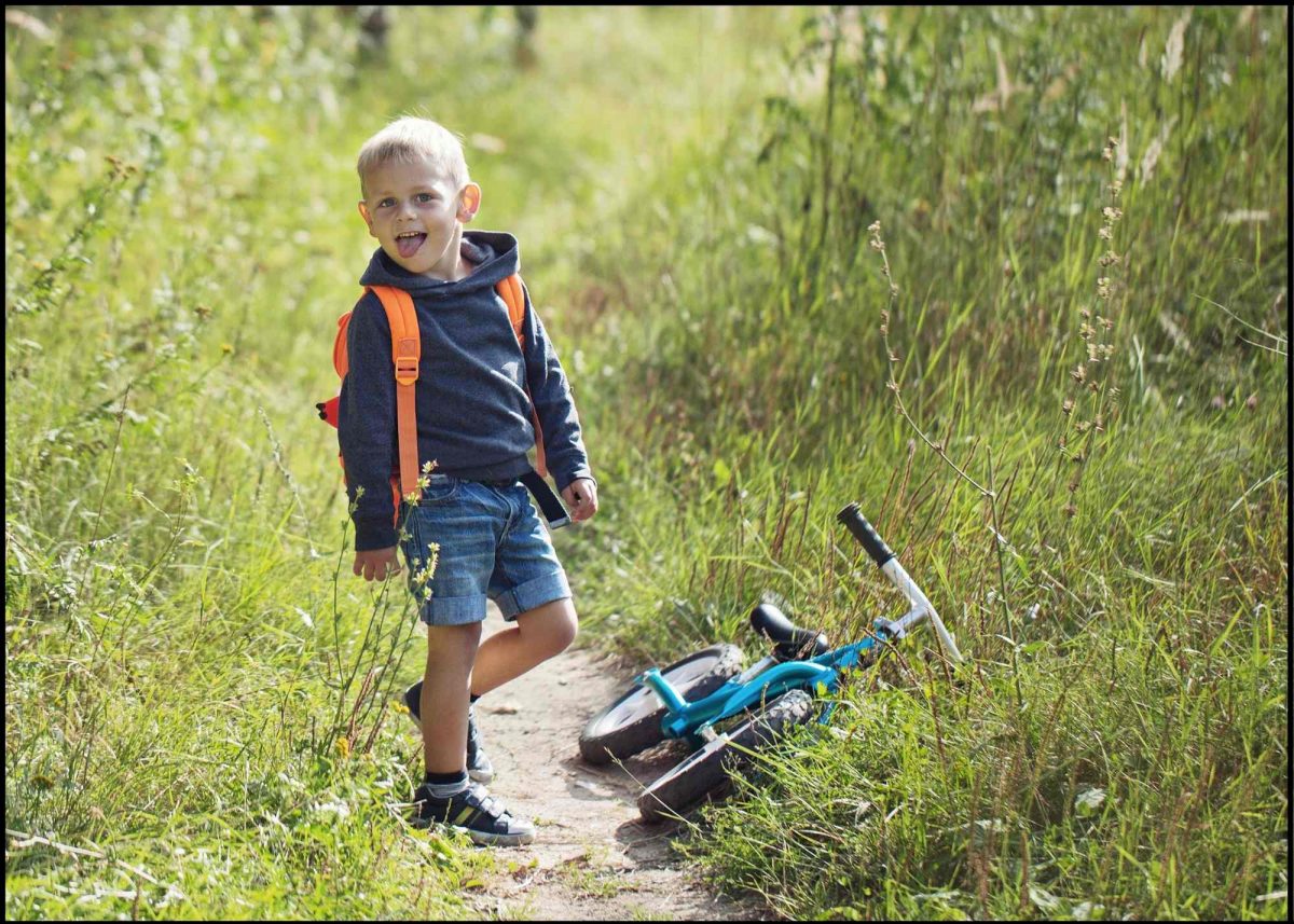 smiling kid with a backpack trail riding with a balance bike